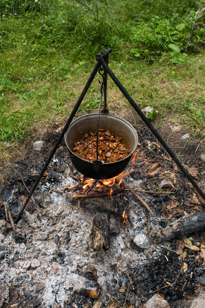 The cooking pot with goulash which is hanging on the tripod above campfire The cooking pot with goulash which is hanging on the tripod above campfire