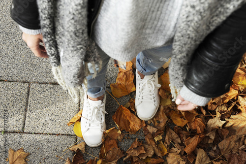 фотографія Young hipster woman is standing among autumn leaver wearing white sneakers