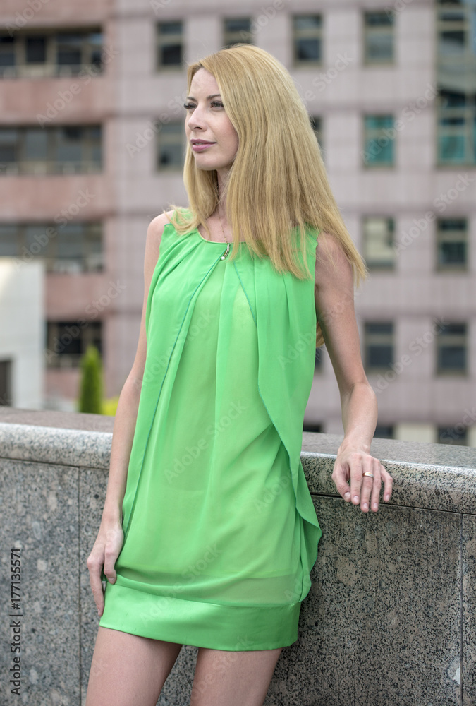 
Beautiful blonde girl in a green short summer dress on the streets of the city
