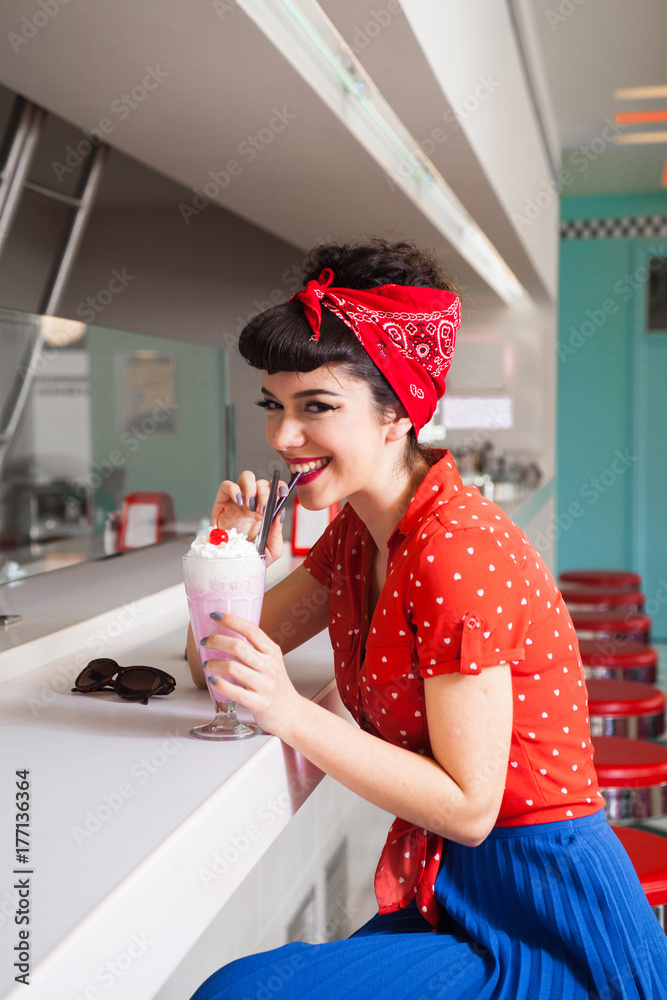 Stylish rockabilly/pin up girl enjoying milkshake at bar. Stock