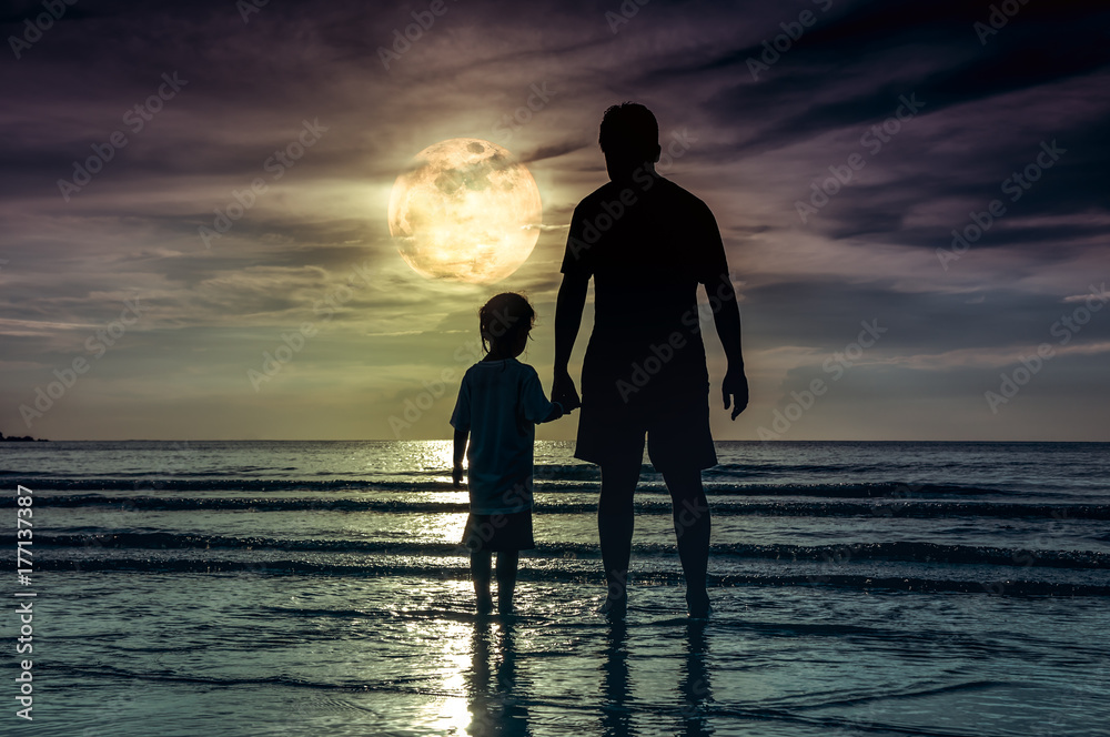 Silhouette of child holding hands her father, standing in the sea.