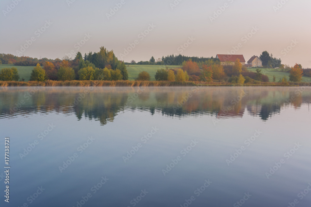 French countryside - Lorraine. A small lake with a farm and autumnal forest in the background.