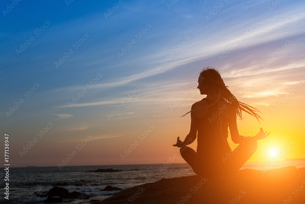Yoga woman silhouette on the ocean during amazing sunset.