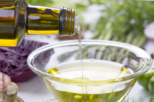 Pouring olive oil into a glass bowl and with fresh vegetable background.