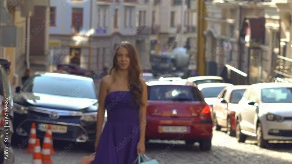 Slow motion. A funny attractive blonde is spinning in the street. The girl is engaged in shopping and carries in the hens mngo bright colored packages from the stores. the girl is dressed in a long Slow motion. A funny attractive blonde is spinning in the street. The girl is engaged in shopping and carries in the hens mngo bright colored packages from the stores. the girl is dressed in a long