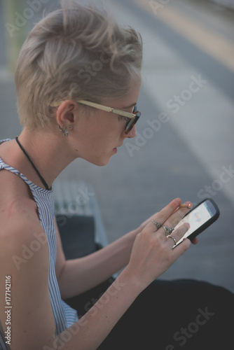 young woman outdoor using smart phone smoking cigarette - technology, social network, communication concept