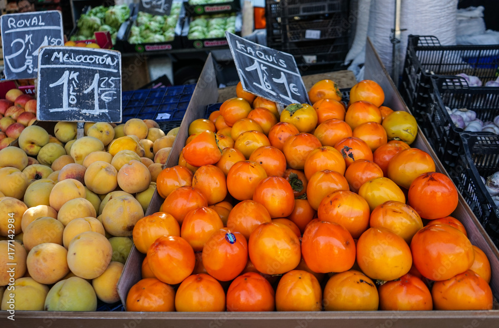 Persimmons and peaches in stack in a vegetables stand in a street market in Madrid, Spain.