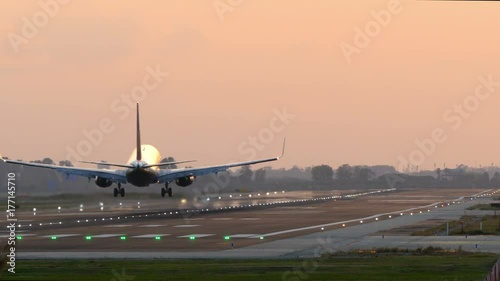 Big plane landing at Barcelona airport seen from behind at sunset with lit signal lights on the runway.  photo