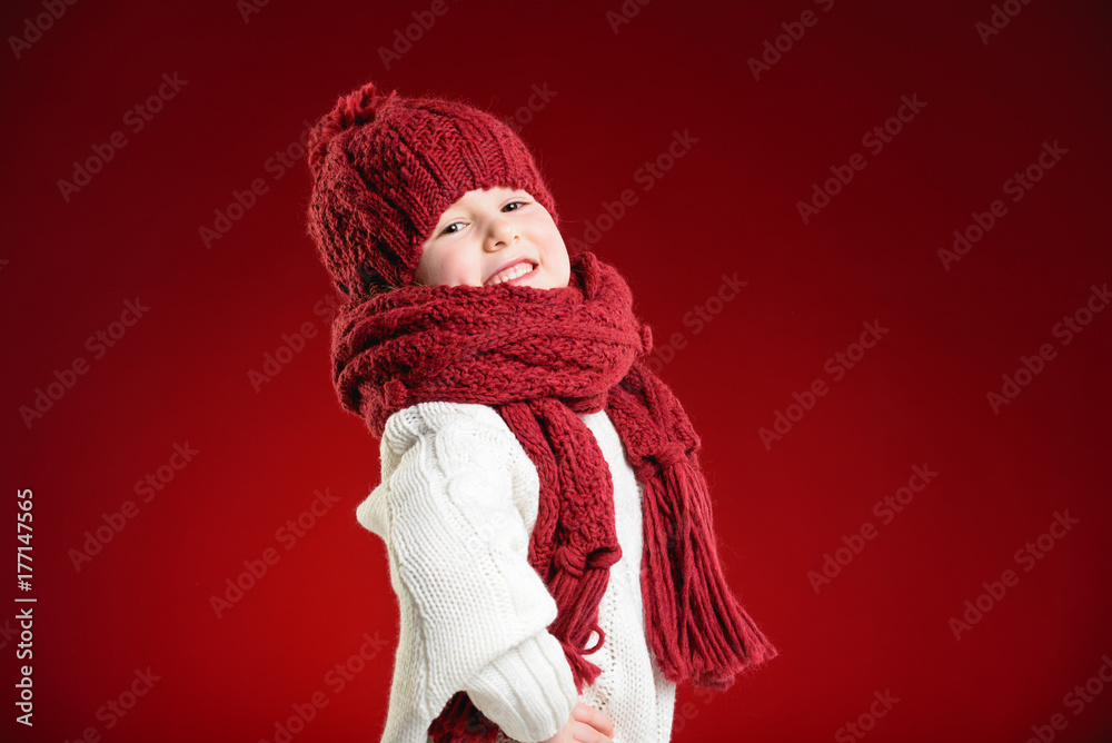 Beautiful blond girl playing in the winter warm hat and scarf on red background Beautiful blond girl playing in the winter warm hat and scarf on red background
