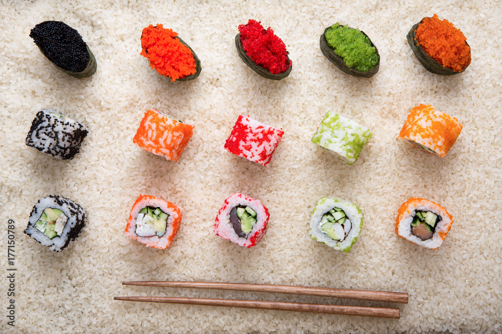 Top view on sushi rolls and gunkan near chopsticks on white rice background and texture, flat lay Top view on sushi rolls and gunkan near chopsticks on white rice background and texture, flat lay