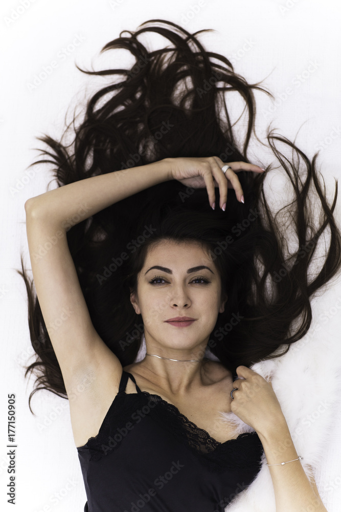 Portrait of the beautiful young brunette woman with long black hair posing lying over light background