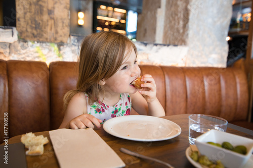 Photography Four years age blonde girl eating croquette with hand next to woman mother sitti