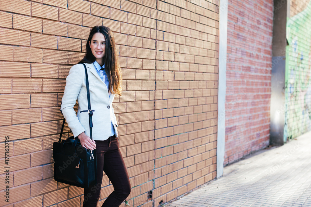 Young businesswoman standing on a brick wall. Young businesswoman standing on a brick wall.
