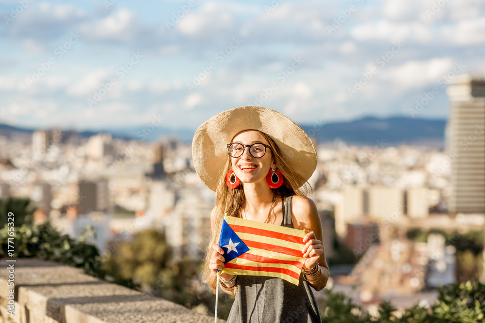 Portrait of young woman tourist sitting with catalan flag on the cityscape background in Barcelona