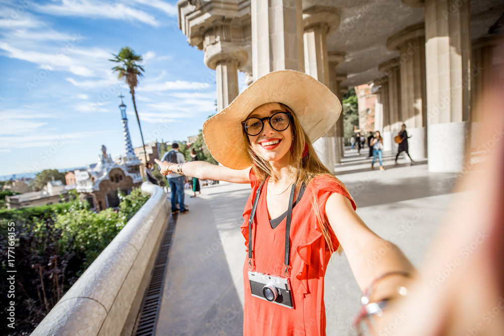 Obraz premium Happy woman tourist in red dress with hat standing near the columns visiting famous Guell park in Barcelona