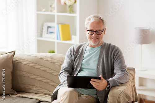 senior man with tablet pc sitting on sofa at home photo