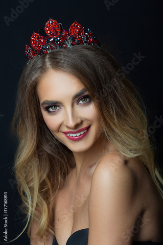 portrait of beautiful young girl with makeup and hairdo with crown on head on black background