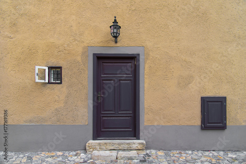 Old wooden door on rustic old world style concrete yellow wall with small window on the side