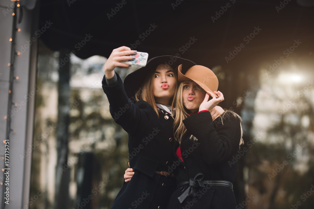 Fashionable women friends in hat make selfie in city