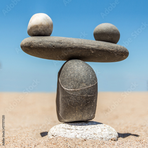 Figure in the form of weights from sea stones on a sandy beach. A square picture.
