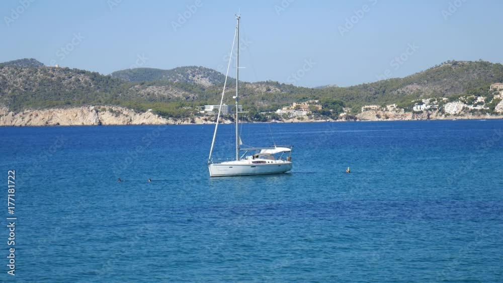 Sailboat floating on small waves on the blue sea with mountain landscape in Cala Pi Mallorca Spain Sailboat floating on small waves on the blue sea with mountain landscape in Cala Pi Mallorca Spain