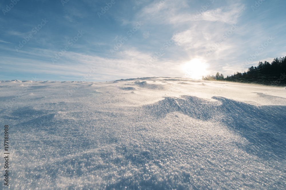 Schneebedeckter Hügel bei starkem Wind der die Flocken über den Hügel fegt Schneebedeckter Hügel bei starkem Wind der die Flocken über den Hügel fegt