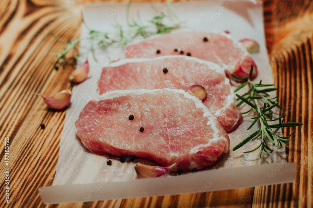 Raw pork steak on a dark wooden table with rosemary and garlic