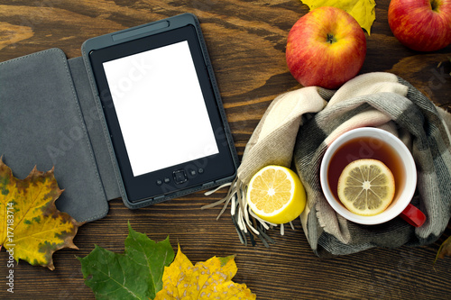 eBook and a cup of hot tea with a lemon wrapped in a scarf on a wooden table