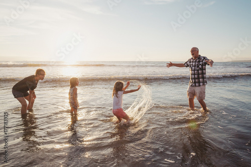 Fun, energetic grandparents playing in waves with young grandkids - girls - at sunset photo