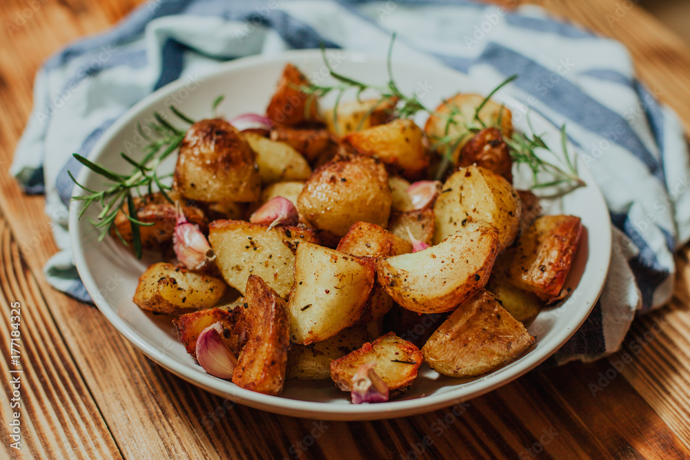 Roasted potato in white plate on wooden background with rosemary and garlic Roasted potato in white plate on wooden background with rosemary and garlic