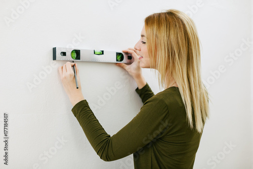 Young woman using level tool for hanging a picture.