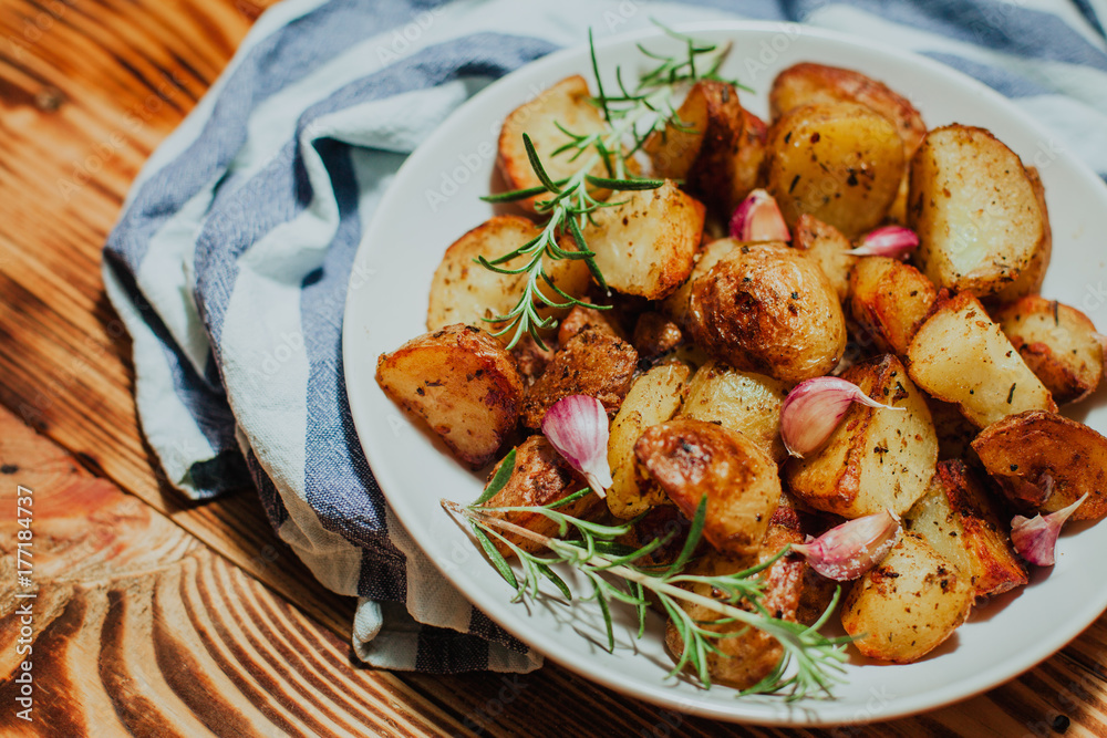 Roasted potato in white plate on wooden background with rosemary and garlic Roasted potato in white plate on wooden background with rosemary and garlic
