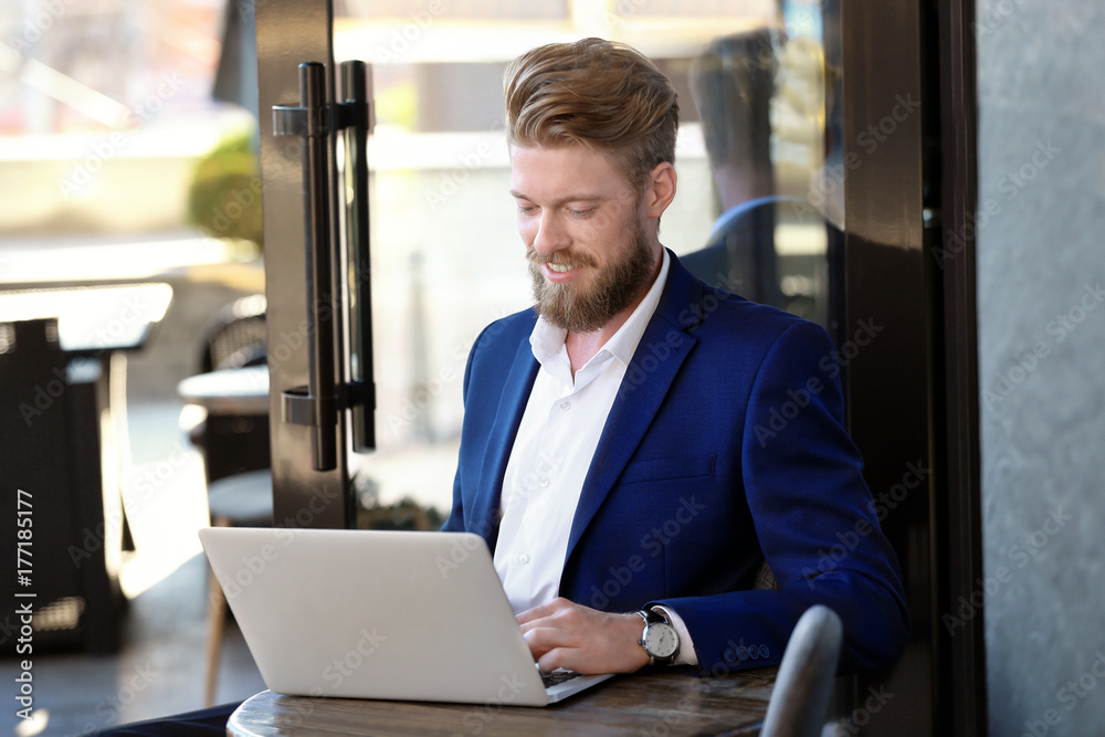 Fototapeta premium Smiling young entrepreneur working on laptop in cafe, business communication and remote work lifestyle