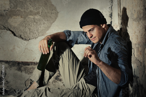 Man sitting with cigarette and bottle of alcohol in abandoned building