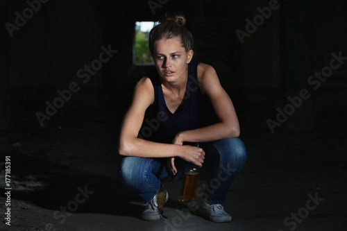 Woman sitting with bottle of alcohol in abandoned building