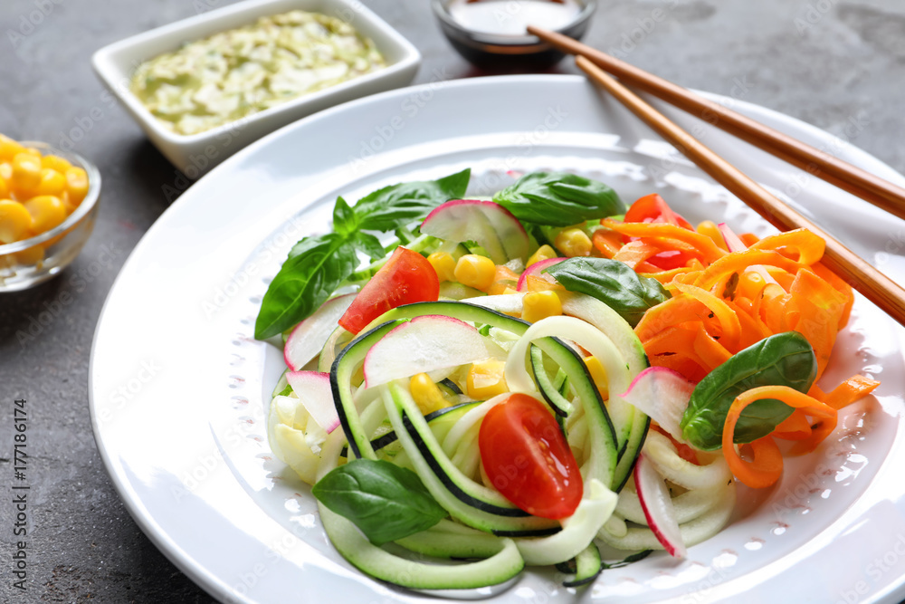 Plate with raw vegetable spaghetti and chopsticks on grunge background Plate with raw vegetable spaghetti and chopsticks on grunge background