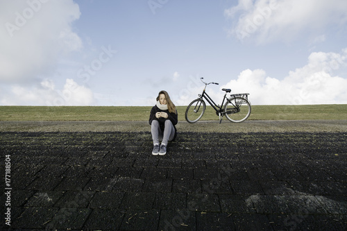 Young woman sits at a dyke and texting with her mobile phone. photo
