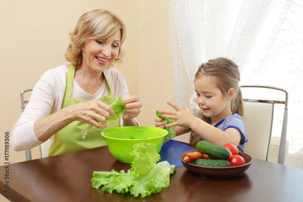 Cute little girl and her grandmother cooking on table