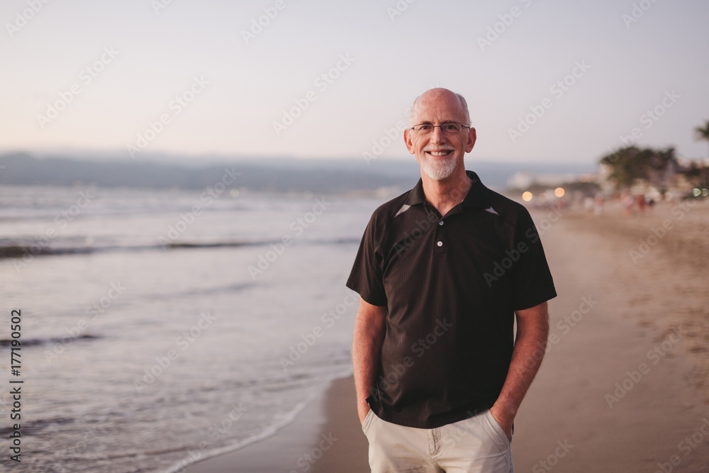 Content middle aged, retired man smiling outside on ocean beach at sunset Content middle aged, retired man smiling outside on ocean beach at sunset