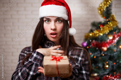 Young cute excited woman in Santa cap with a gift box in hand. New Year, Christmas, gift, surprise, celebration, emotions concept