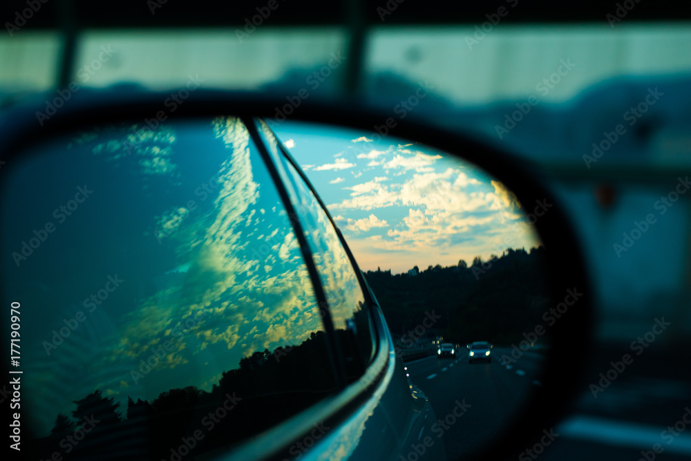 Ultimate roadtrip : car mirror picture of high speed highway road, cars, and nature in evening sky