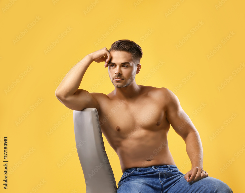 Sexy shirtless man sitting on chair against color background
