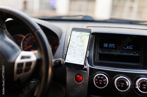 The map on the phone in the background of the dashboard. Black mobile phone with map gps navigation fixed in the mounting. Map for travel. © korchemkin