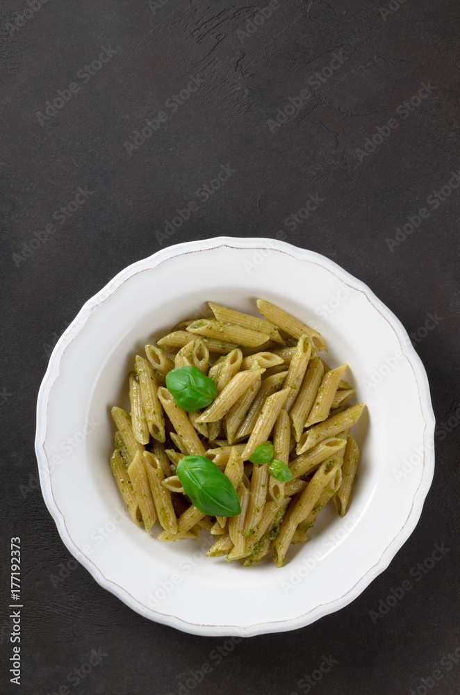 Pasta with homemade pesto sauce in a white plate on a dark stone slate background, vertical image, top view, copy space