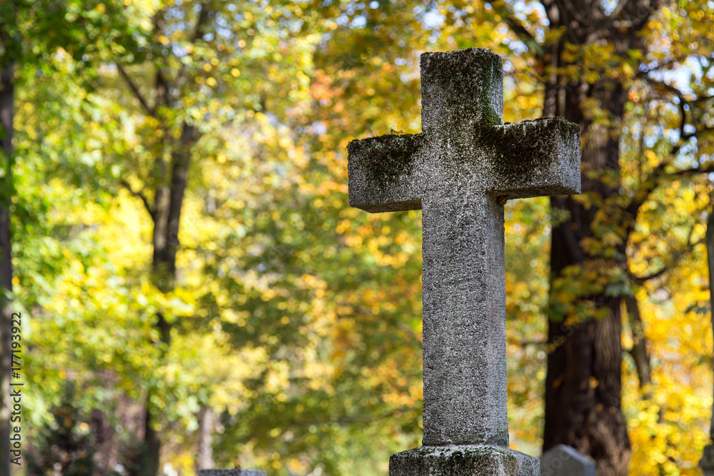 Stary kamienny krzyż na cmentarzu w otoczeniu jesiennych drzew. Symbol chrześcijaństwa