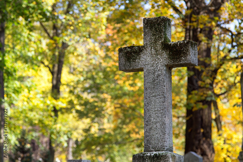 Stary kamienny krzyż na cmentarzu w otoczeniu jesiennych drzew. Symbol chrześcijaństwa