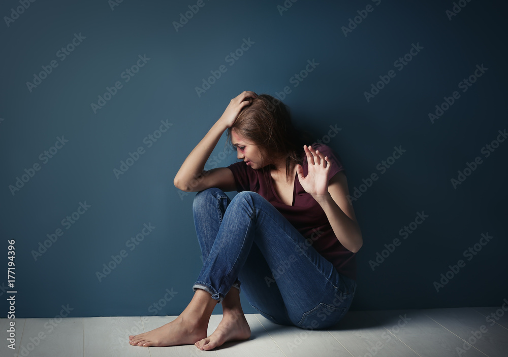 Battered young woman sitting near blue wall Battered young woman sitting near blue wall