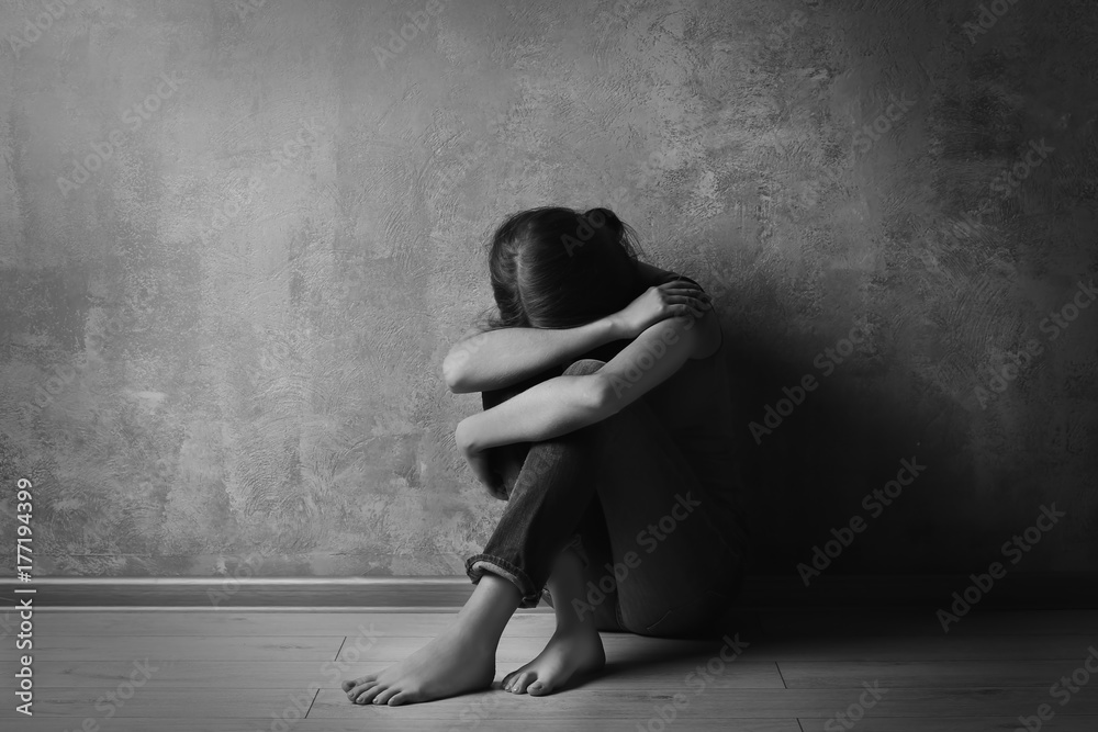Fototapeta premium Battered young woman sitting near concrete wall