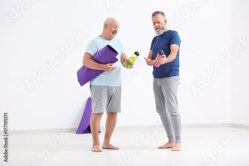 Men with bottles of water and yoga mat indoors