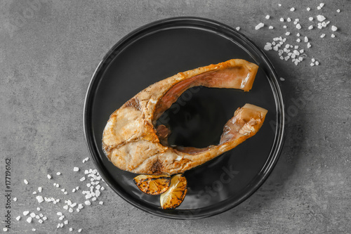 Black plate with fried fish steak on grey background